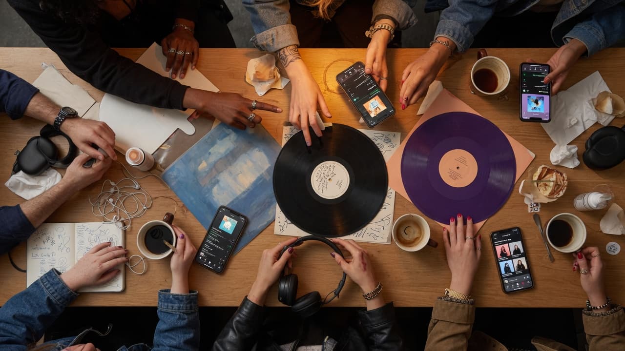 Artists and fans gathered around a table with vinyl records, headphones, and phones — a moment of connection